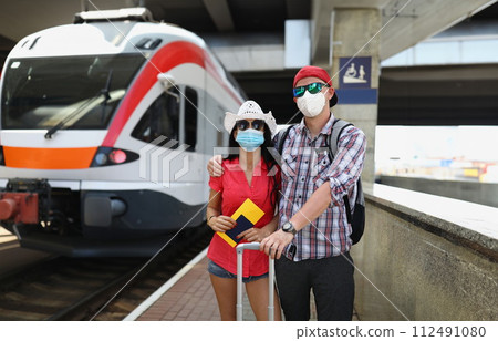 Young couple in protective medical masks standing near train with tickets in their hands 112491080