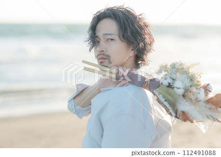 A man in his 30s wearing a white shirt standing by the seaside 112491088