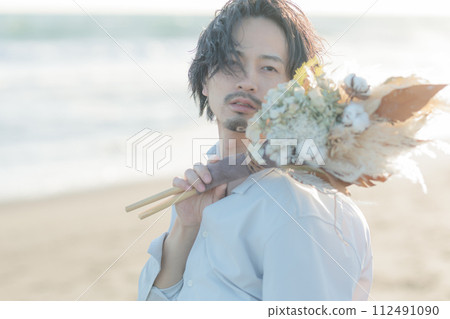 A man in his 30s wearing a white shirt standing by the seaside 112491090