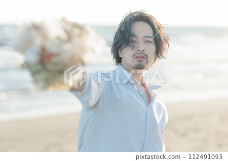 微笑的男人在海灘上遞上一束鮮花 |適用於婚禮和生活方式廣告 微笑的男人在海灘上遞上一束鮮花 |適用於婚禮和生活方式廣告 112491093