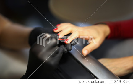 Manicurist painting woman nails with red varnish closeup Manicurist painting woman nails with red varnish closeup 112491094