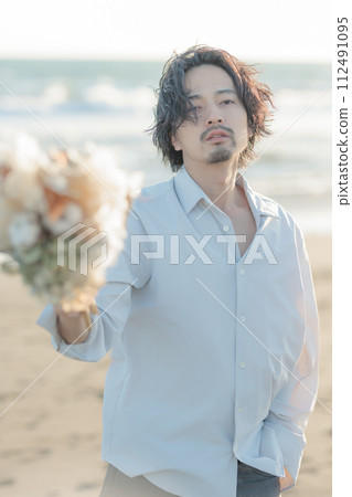 A man in his 30s wearing a white shirt standing by the seaside A man in his 30s wearing a white shirt standing by the seaside 112491095