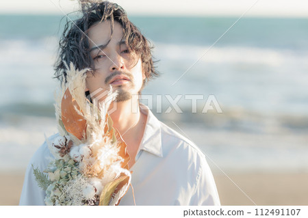 A man in his 30s wearing a white shirt standing by the seaside A man in his 30s wearing a white shirt standing by the seaside 112491107