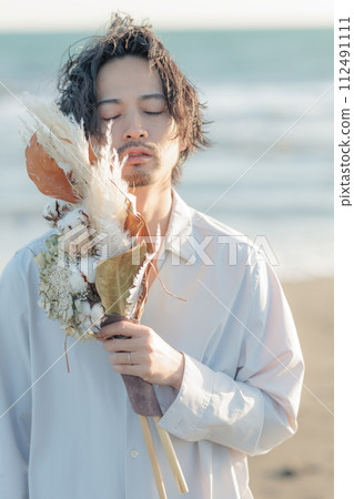A man in his 30s wearing a white shirt standing by the seaside 112491111