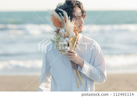 A man in his 30s wearing a white shirt standing by the seaside 112491114