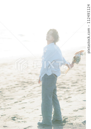 A man in his 30s wearing a white shirt standing by the seaside 112491124