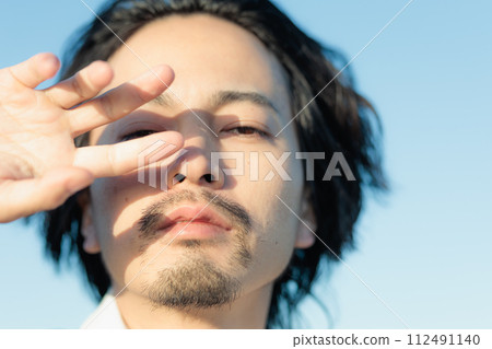 A man in his 30s wearing a white shirt standing by the seaside 112491140