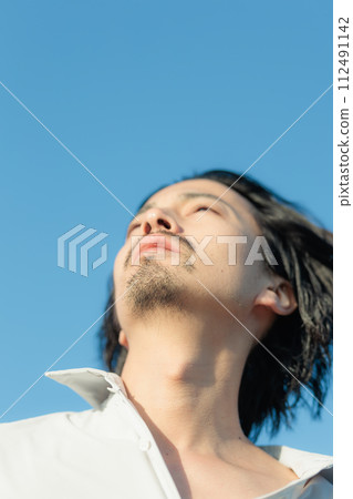 A man in his 30s wearing a white shirt standing by the seaside A man in his 30s wearing a white shirt standing by the seaside 112491142