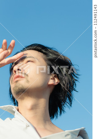 A man in his 30s wearing a white shirt standing by the seaside 112491143