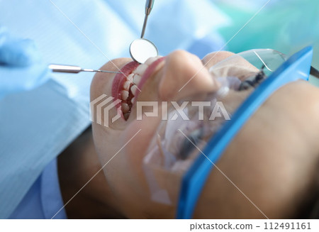 Dentist examining oral cavity of woman patient in clinic using tools closeup Dentist examining oral cavity of woman patient in clinic using tools closeup 112491161