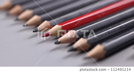 Closeup of one red wooden pencil among many black background 112491214