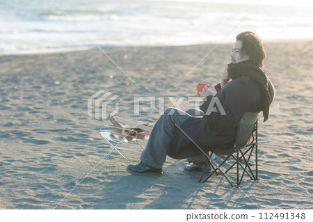A man in his 30s having a bonfire at the beach A man in his 30s having a bonfire at the beach 112491348