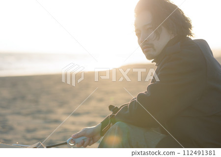 A man in his 30s having a bonfire at the beach 112491381