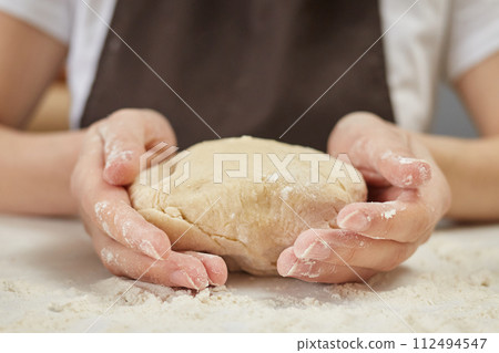Unrecognizable woman wearing brown apron holding dough for baking bread sitting at bakery workplace Unrecognizable woman wearing brown apron holding dough for baking bread sitting at bakery workplace 112494547