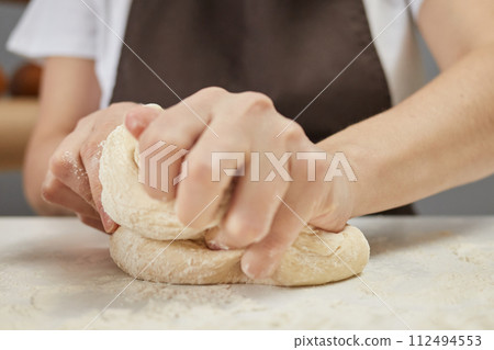 Unknown woman wearing brown apron kneading dough on table sprinkled with flour preparing for baking bread 112494553