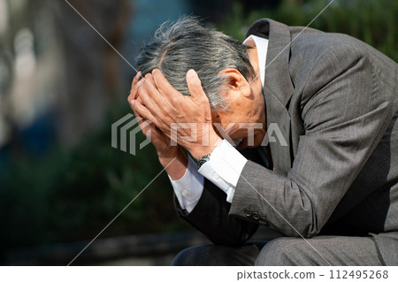 穿著西裝的老人坐著，抱著頭 112495268