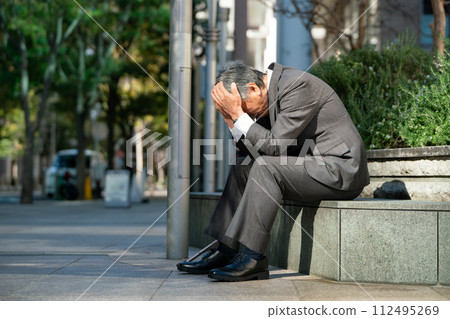 穿著西裝的老人坐著，抱著頭 112495269