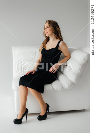 Woman in black dress sitting on white leather sofa. Concept of beauty and perfection 112496271