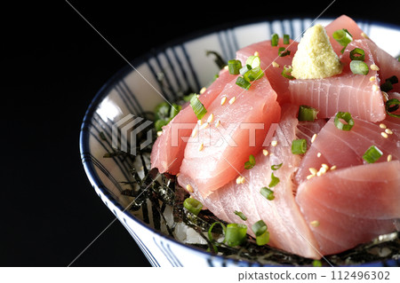 Photograph of bowl of chopped tuna against a black background 112496302