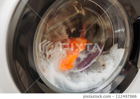 Closeup of washing machine door with spinning laundry Closeup of washing machine door with spinning laundry 112497866