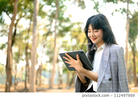 Young businesswoman using digital tablet while sitting on bench in the autumn park 112497989