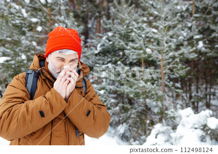 Man in a winter forest looking sick and got running nose Man in a winter forest looking sick and got running nose 112498124