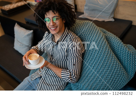 Top view of a young curly-haired man having coffee and smiling Top view of a young curly-haired man having coffee and smiling 112498232