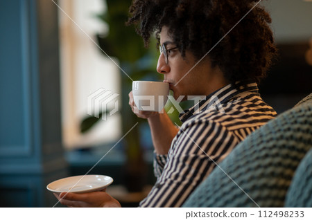 Smiling young man in striped shirt having coffee Smiling young man in striped shirt having coffee 112498233