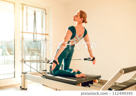 Flexible and slim woman doing stretching exercises on Pilates machine 112499395