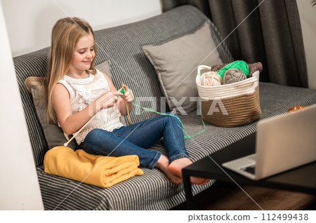 Little girl to knit while sitting on couch enjoying her hobby 112499438