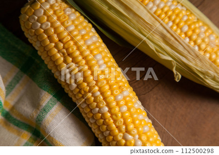 Close up view of three cobs sweet corn with green leaves on wooden background.. 112500298