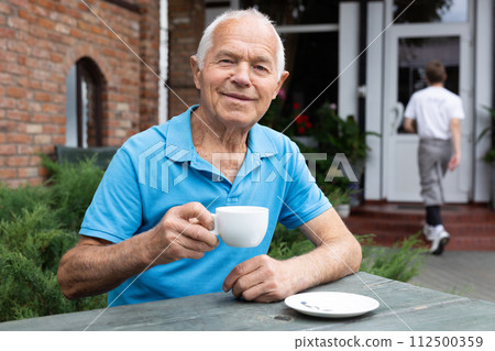 Old man sitting at table in outdoor cafe and drinking tea 112500359