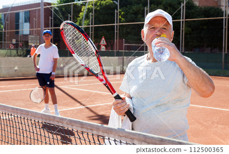 Mature man drink water on tennis court 112500365