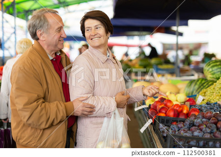Mature casual man and woman picking fresh organic fruits during shopping at local market 112500381