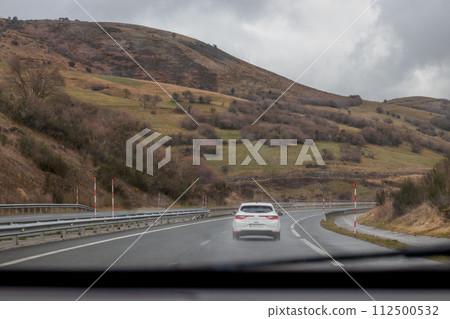 White car on highway with mountains and clouds in background 112500532