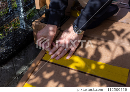 A man attaching anti-slip to a wooden deck sloop A man attaching anti-slip to a wooden deck sloop 112500556