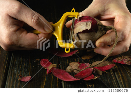 A chef using a peeler peels beta vulgaris to prepare a national dish for breakfast. Delicious vegetable diet concept A chef using a peeler peels beta vulgaris to prepare a national dish for breakfast. Delicious vegetable diet concept 112500676