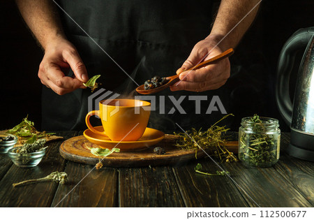 A man brews healthy tea from medicinal dry herbs. A hand holds a spoon with dry rose hips to add to a cup. Traditional medicine concept A man brews healthy tea from medicinal dry herbs. A hand holds a spoon with dry rose hips to add to a cup. Traditional medicine concept 112500677