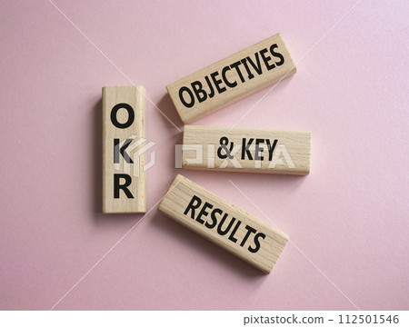 OKR objectives and key results symbol. Wooden blocks with words OKR objectives and key results. Beautiful pink background. Business and OKR concept. Copy space. OKR objectives and key results symbol. Wooden blocks with words OKR objectives and key results. Beautiful pink background. Business and OKR concept. Copy space. 112501546