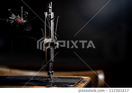 An old sewing machine stands on the table at home ready to work and sew. Classic retro style manual sewing machine ready for sewing work. The machine is old style made of metal with floral patterns 112501817