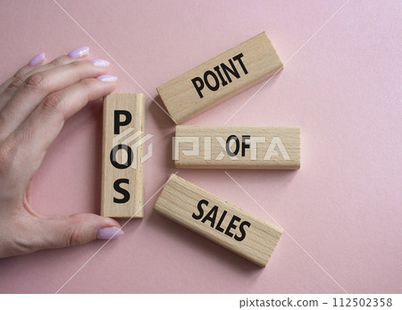 POS - Point Of Sales symbol. Wooden cubes with words POS. Businessman hand. Beautiful pink background. Business and POS concept. Copy space. 112502358