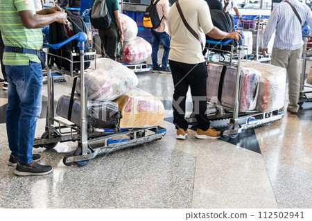 Passenger travelers at airport with luggages on trolley wrapped with protective film Passenger travelers at airport with luggages on trolley wrapped with protective film 112502941