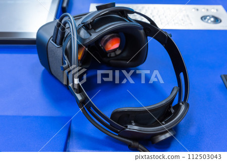 Black VR headset with red visors lays on blue desk, rear view 112503043