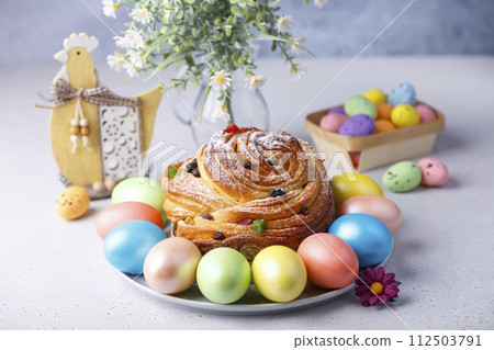 Craffin (Cruffin) with raisins and candied fruits sprinkled with powdered sugar. Traditional Easter Bread Kulich and painted eggs on a gray background. Easter Holiday. Close-up, selective focus. Craffin (Cruffin) with raisins and candied fruits sprinkled with powdered sugar. Traditional Easter Bread Kulich and painted eggs on a gray background. Easter Holiday. Close-up, selective focus. 112503791