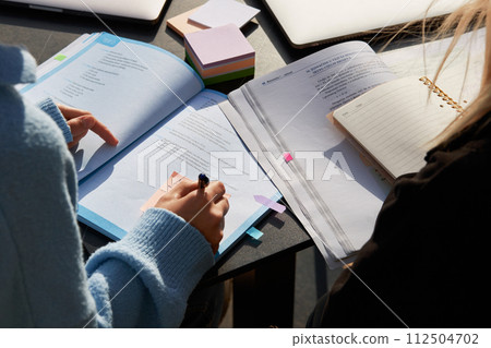 A student's hand writes with a ballpoint pen on note paper in a textbook. Close-up 112504702