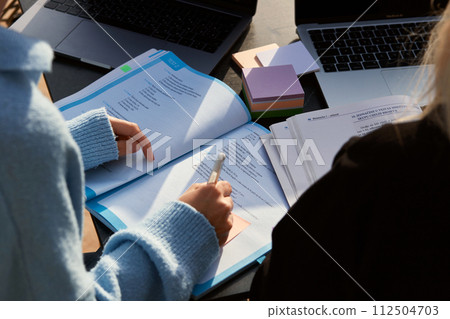 A student's hand writes with a ballpoint pen on note paper in a textbook. Close-up 112504703
