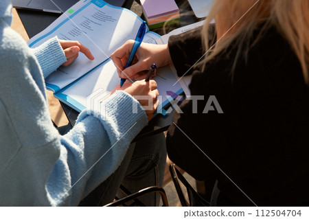 A student's hand writes with a ballpoint pen on note paper in a textbook. Close-up A student's hand writes with a ballpoint pen on note paper in a textbook. Close-up 112504704