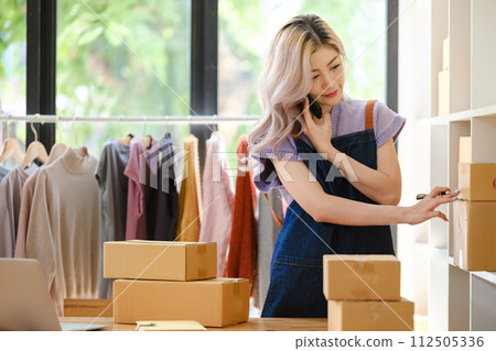 Online shopping concept, Female entrepreneur talks on smartphones and confirm orders with customers. Online shopping concept, Female entrepreneur talks on smartphones and confirm orders with customers. 112505336