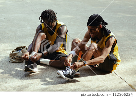 Cheerful Black men tying shoe laces before game of streetball Cheerful Black men tying shoe laces before game of streetball 112506224