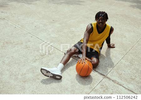 Black streetball player resting on ground after game and smiling at camera 112506242